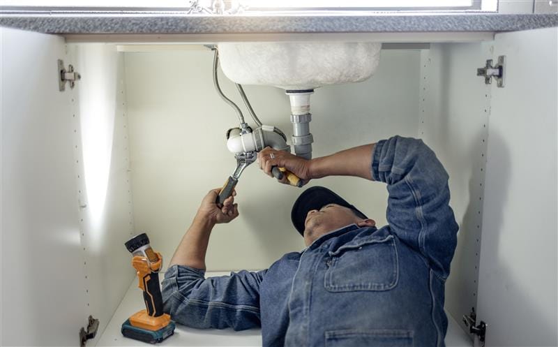 Plumber repairing pipes beneath a bathroom sink in Lakeland