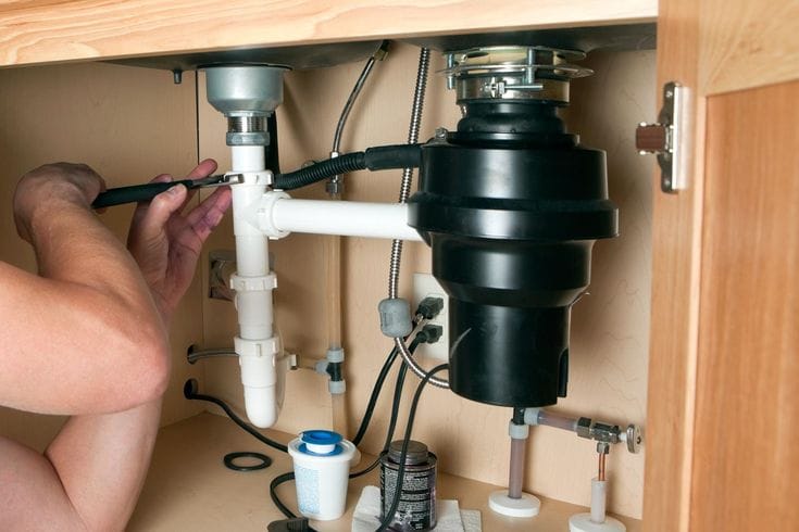 Plumber installing a garbage disposal beneath a kitchen sink in Lakeland