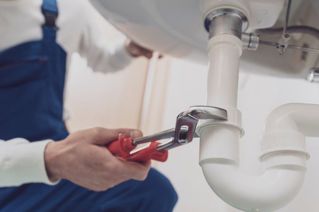 Plumber repairing a white drain pipe beneath a sink in Lakeland